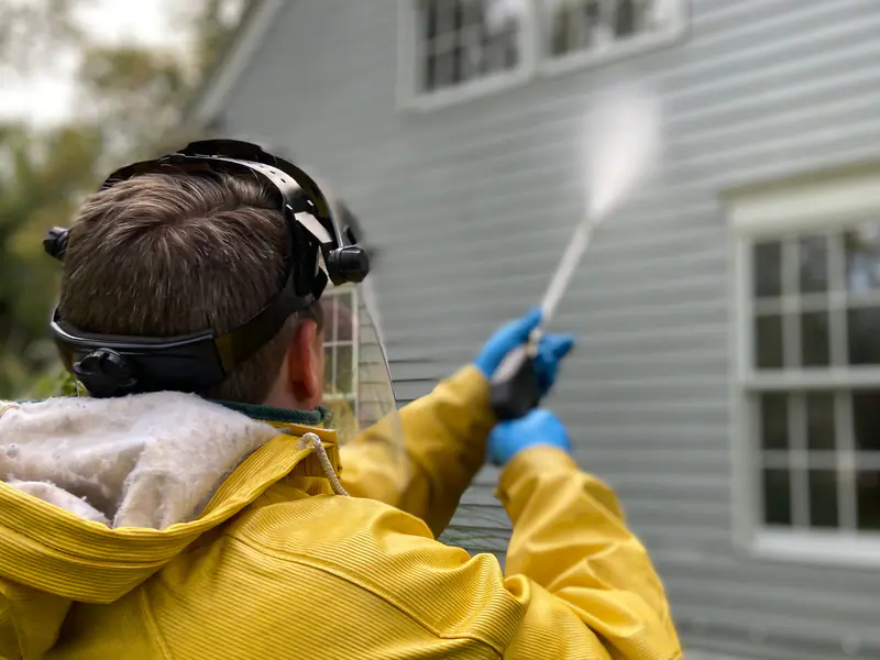 Worker in a rain jacket pressure-washing gray lap siding