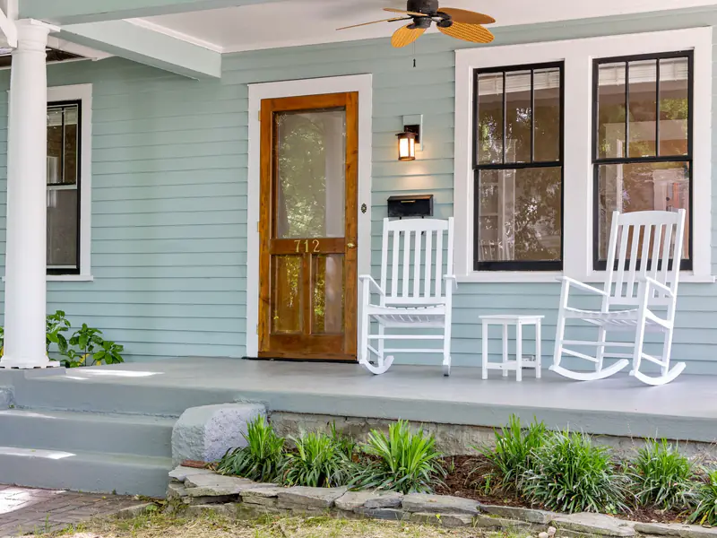 Front porch with pale blue siding, a stained wood door and white rocking chairs