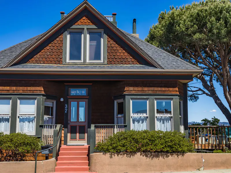 Shingled bungalow with green trim, bay windows and red front steps