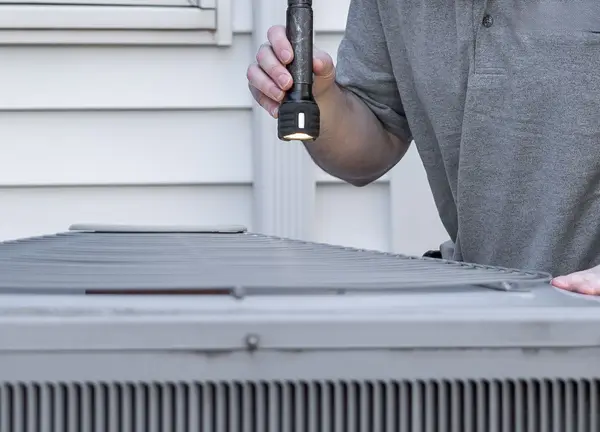 Technician with a flashlight checking an outdoor AC unit