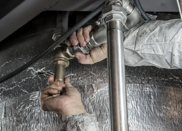 Plumber's hands tightening a brass fitting on a water line