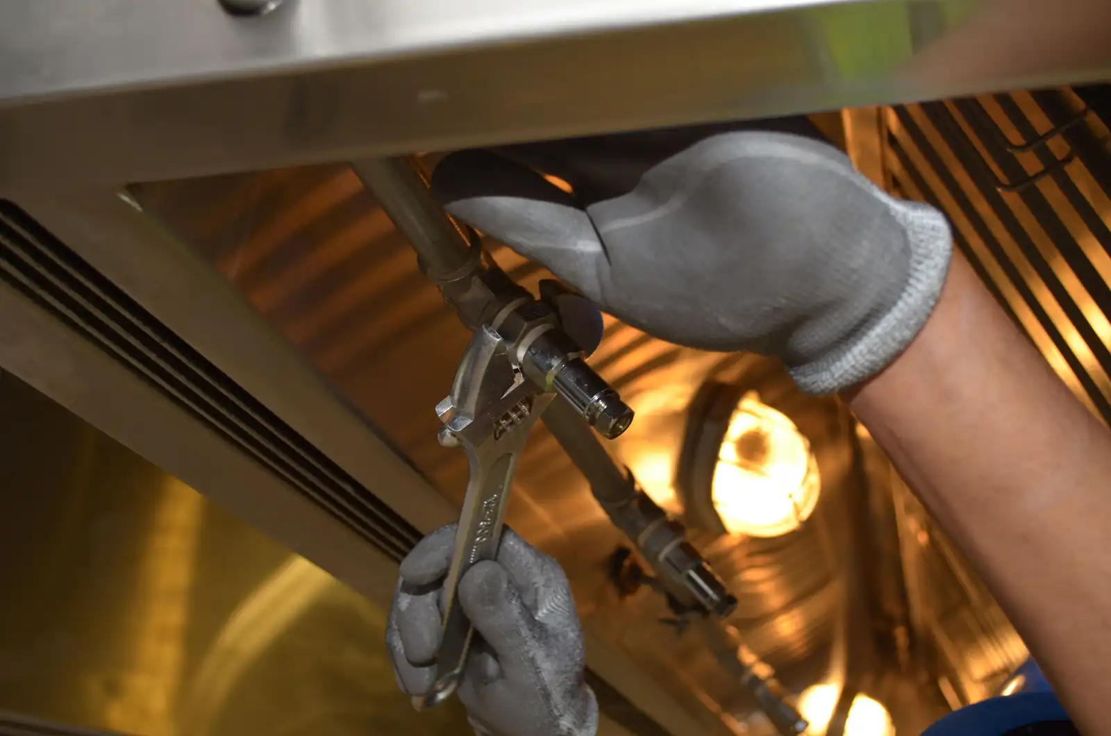 Gloved hands tightening pipe joints with a wrench